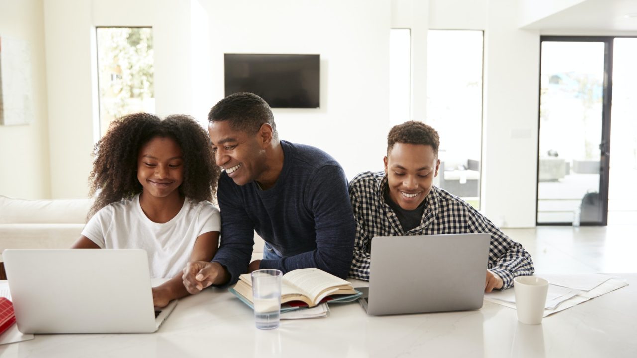 Smiling dad helping his teen kids with their homework, front view, close up